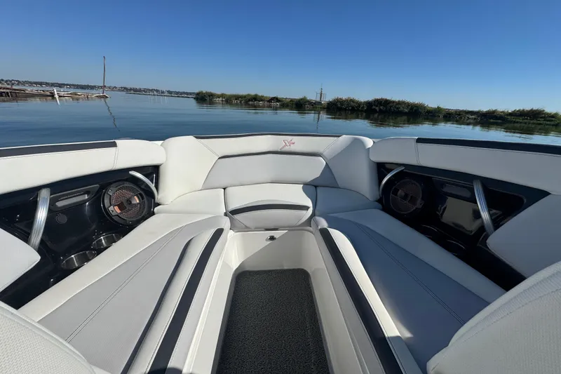 Slide: The Image of 2018 MasterCraft XStar boat interior with sleek seating and speakers, on a calm lake. - 9