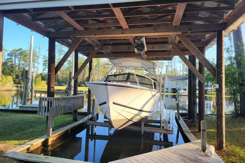Slide: The Image of 1996 Albemarle 24 Express Cuddy Cabin boat docked under wooden shelter by a serene lake. - 2
