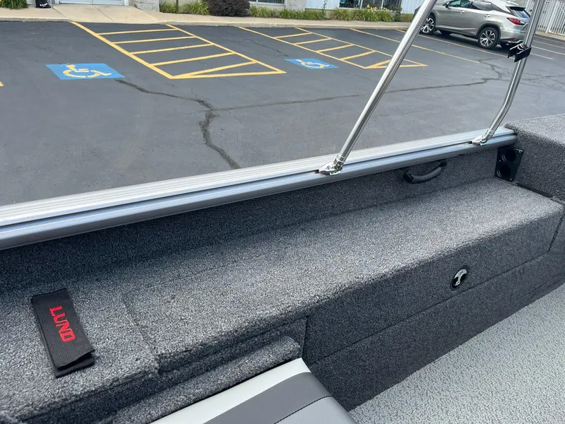 Slide: The Image of 2026 Lund 1875 Impact XS Sport boat interior with gray upholstery and parking lot background. - 19