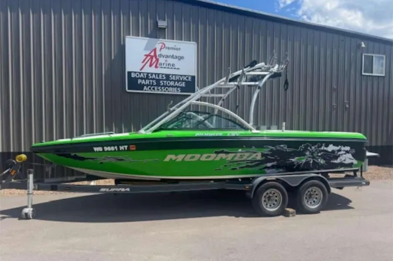 The Image of 2011 Moomba Mobius LSV boat in vibrant green on trailer outside marine shop. - 0