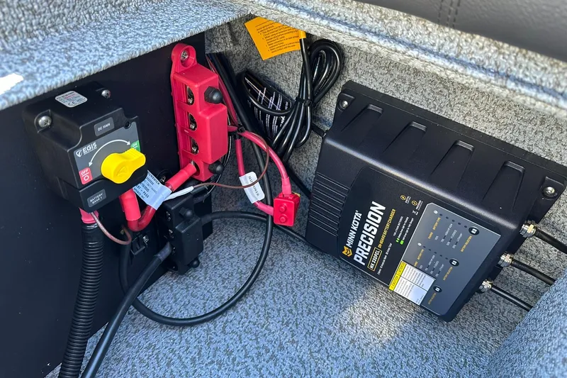 Slide: The Image of Electrical components inside a 2026 Lund 1875 Impact XS Sport boat, featuring a Minn Kota Precision charger. - 26