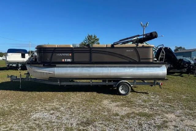 The Image of 2020 Harris Cruiser 210 pontoon boat on trailer, parked on grassy area under clear blue sky. - 1