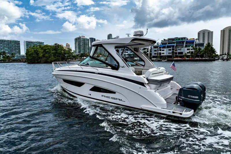 The Image of 2021 Regal 33 OBX boat cruising on water with cityscape background. - 1