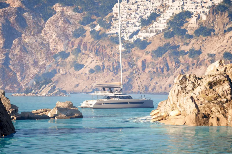 Slide: The Image of Fountaine Pajot 70 S yacht in scenic coastal waters, surrounded by rocky cliffs, 2027 model. - 3