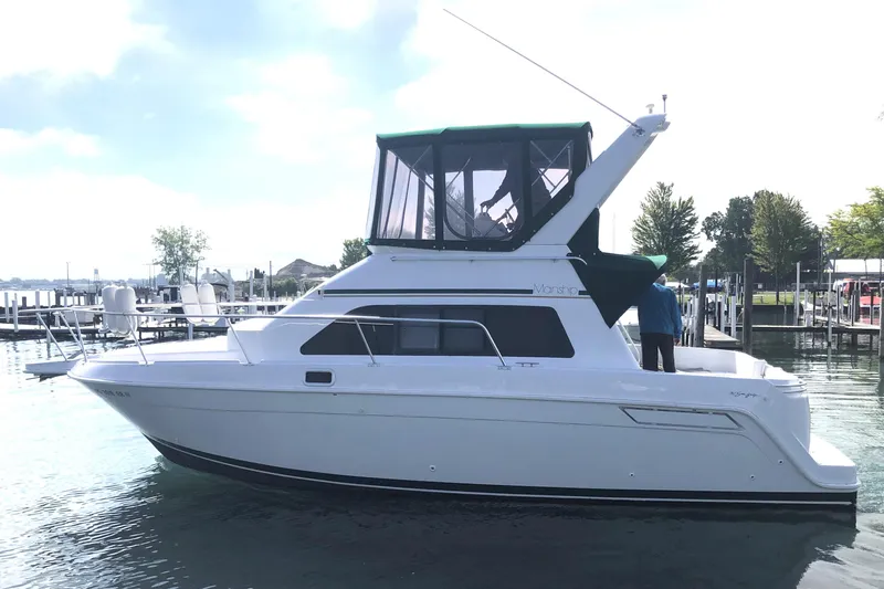 Slide: The Image of 1999 Mainship 31 Sedan Bridge boat docked on calm water, featuring a green canopy. - 4