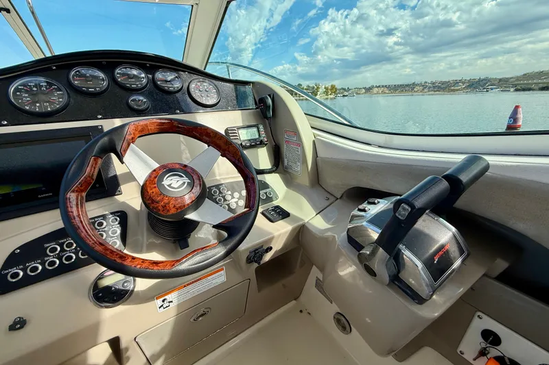 Slide: The Image of 2006 Sea Ray 290 Sundancer helm with steering wheel and controls, overlooking a scenic water view. - 26