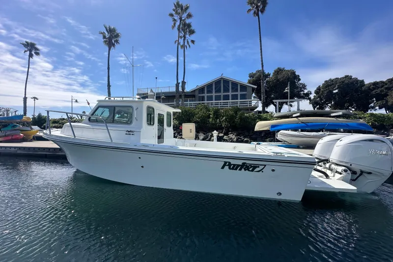 Slide: The Image of 2025 Parker 2420 Sport Cabin boat docked near palm trees and waterfront building. - 2