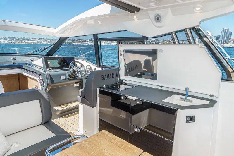 Slide: The Image of 2024 Bavaria SR38 yacht interior with helm, seating, and kitchenette overlooking the ocean. - 23