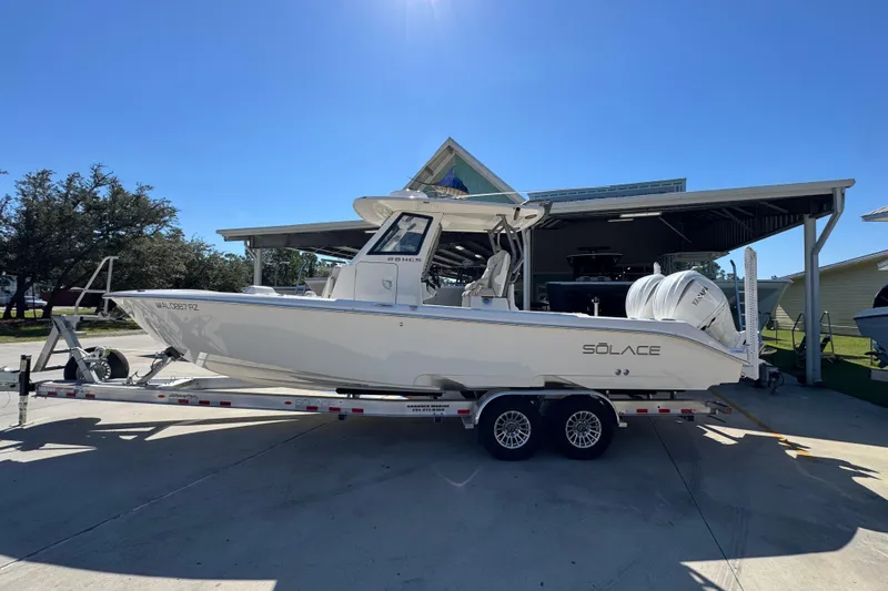 The Image of 2025 Solace 28 HCS boat on trailer, parked outdoors under clear blue sky. - 1