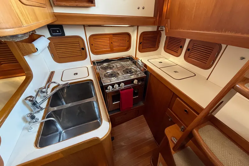 Slide: The Image of Compact 1985 Mason 33 yacht kitchen with dual sinks, stove, and wooden cabinetry. - 13