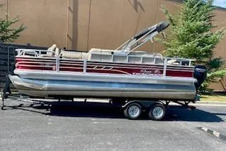 Slide: The Image of 2023 Sun Tracker Fishin' Barge 20 DLX pontoon boat on trailer, parked outdoors. - 2