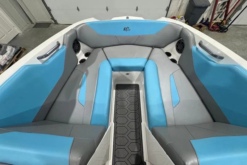 Slide: The Image of 2020 MasterCraft NXT22 boat interior with blue and gray seating, featuring cup holders and speakers. - 12