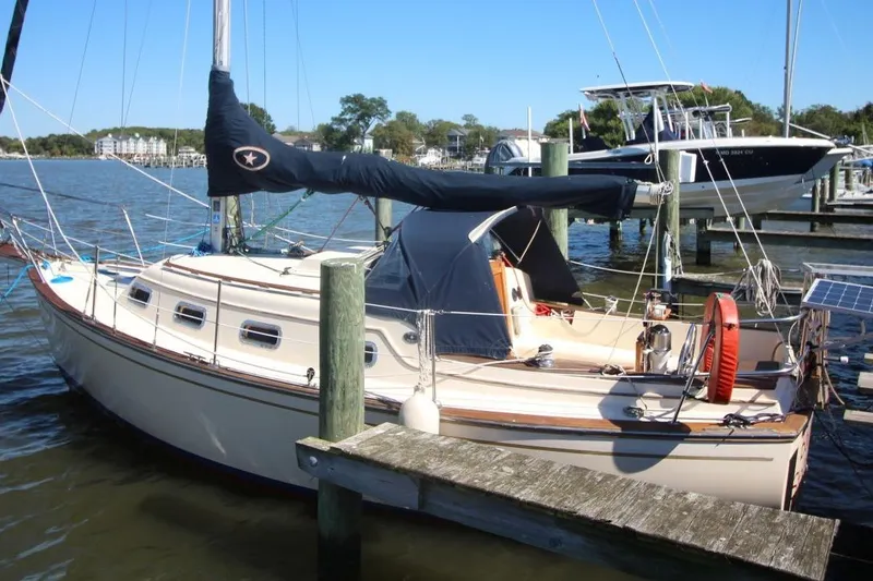 The Image of 1990 Island Packet 27 sailboat docked at a marina, featuring a covered cockpit. - 0