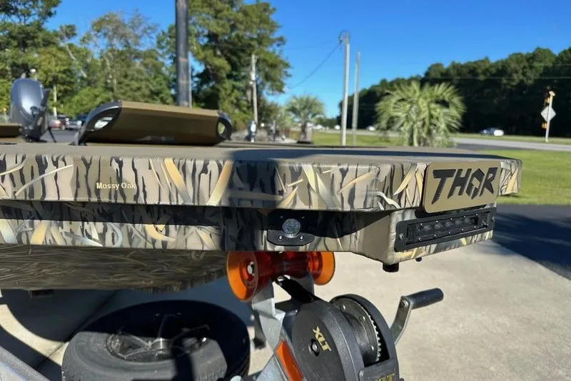 Slide: The Image of 2026 Thor 1754 Timber Hammer boat with camo design and branding, parked outdoors. - 4
