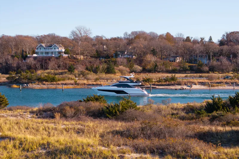 Slide: The Image of 2025 Fairline Squadron 58 yacht cruising on a scenic river with houses in the background. - 111