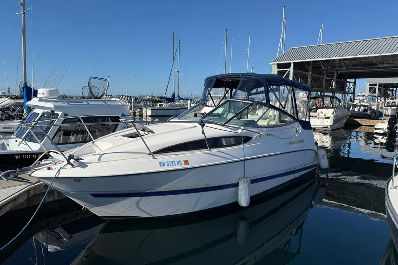 The Image of 2006 Bayliner 245 Cruiser docked at marina, clear blue sky, calm water reflections. - 0
