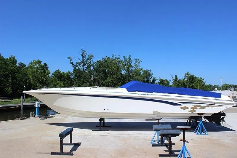 Slide: The Image of 2000 Fountain 32 Fever speedboat with blue cover on dry dock. - 2