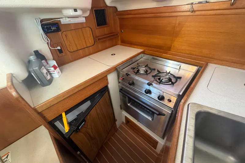 Slide: The Image of Compact kitchen in a 2006 Catalina 309 sailboat with stove, sink, and wooden cabinetry. - 49