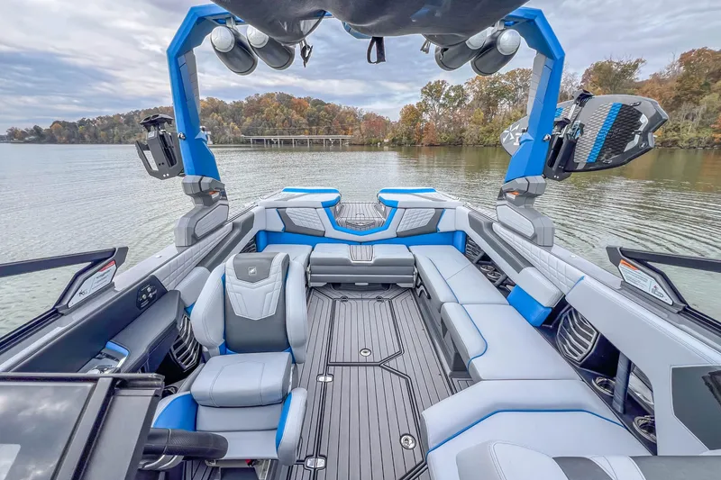 Slide: The Image of 2022 Nautique Super Air Nautique G23 boat interior with blue and gray seating on a calm lake. - 21
