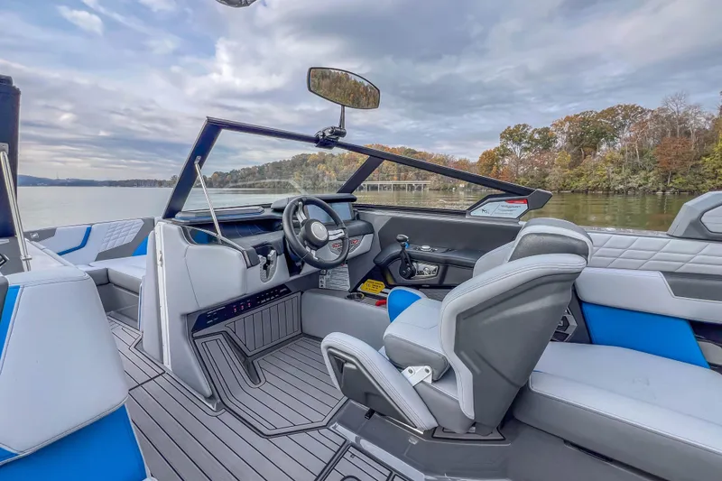 Slide: The Image of 2022 Nautique Super Air Nautique G23 boat interior with modern seating and steering, on a calm lake. - 27