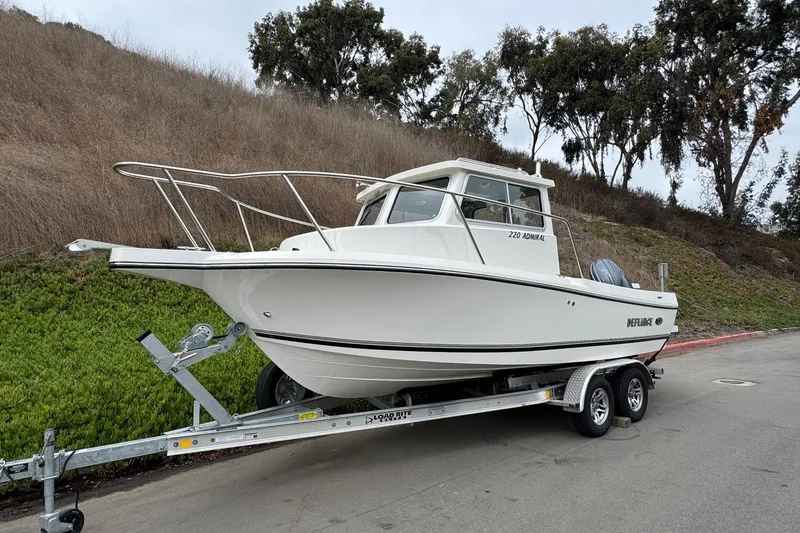 Slide: The Image of 2026 Defiance Admiral 220 EX boat on trailer, parked roadside with grassy hill background. - 4