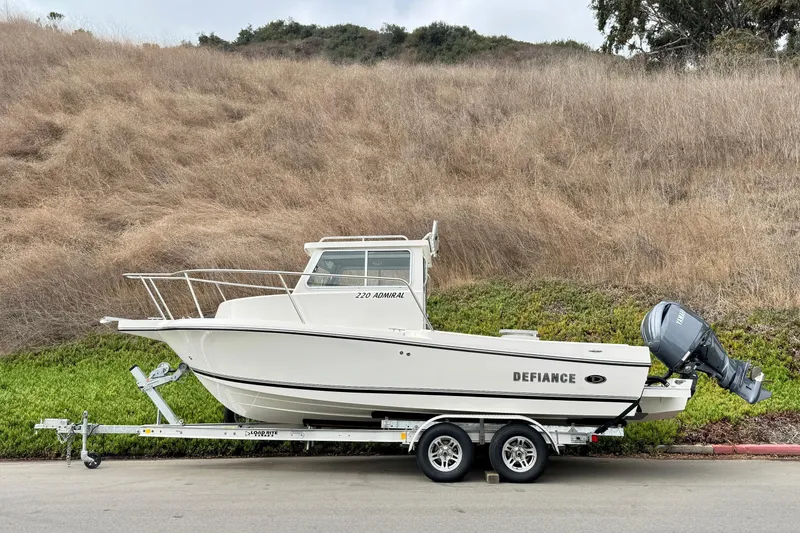 Slide: The Image of 2026 Defiance Admiral 220 EX boat on trailer, parked roadside with grassy hill background. - 66