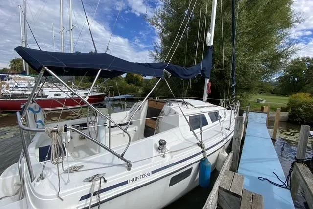 The Image of 1990 Hunter 27 sailboat docked, featuring a blue canopy and white hull. - 1