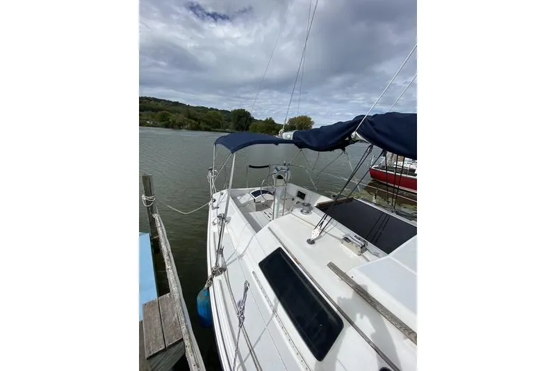 Slide: The Image of 1990 Hunter 27 sailboat docked on a calm lake under cloudy skies. - 4