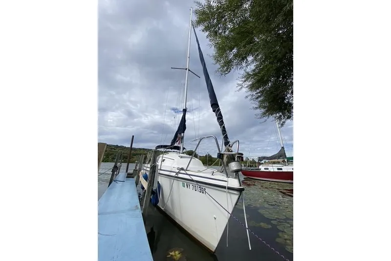 Slide: The Image of 1990 Hunter 27 sailboat docked on a cloudy day, surrounded by water and greenery. - 5