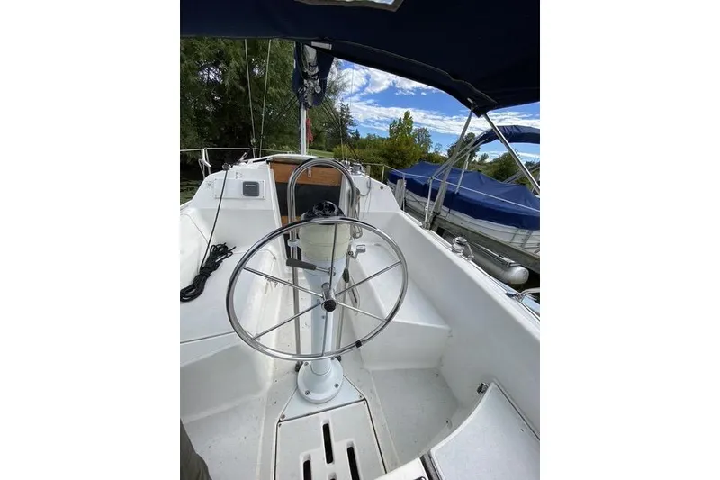 Slide: The Image of 1990 Hunter 27 sailboat cockpit with steering wheel, docked near trees and blue sky. - 8
