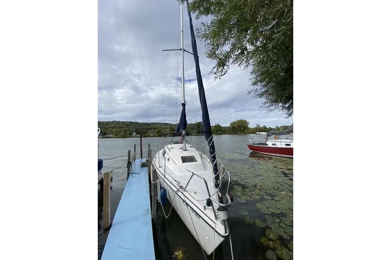 Slide: The Image of 1990 Hunter 27 sailboat docked on a serene lake with cloudy skies. - 9