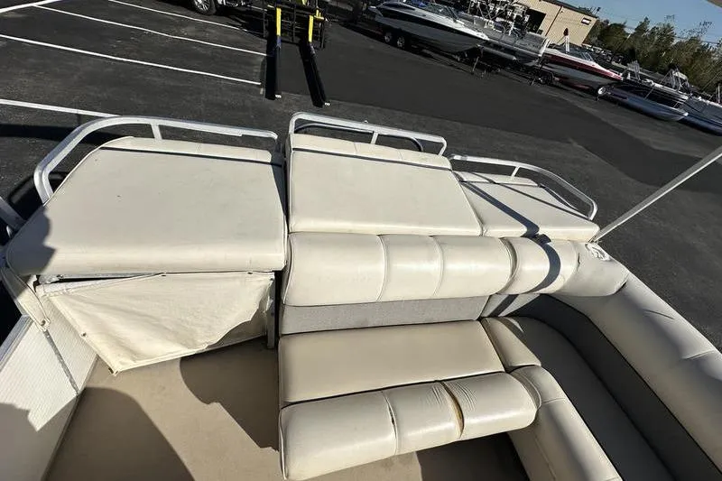 Slide: The Image of 1997 Harris 240 pontoon boat interior with white cushioned seating in a parking lot. - 4