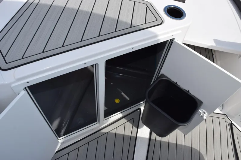 Slide: The Image of 2026 Yamaha Boats 222 FSH Sport E storage compartment with open doors and trash bin. - 15