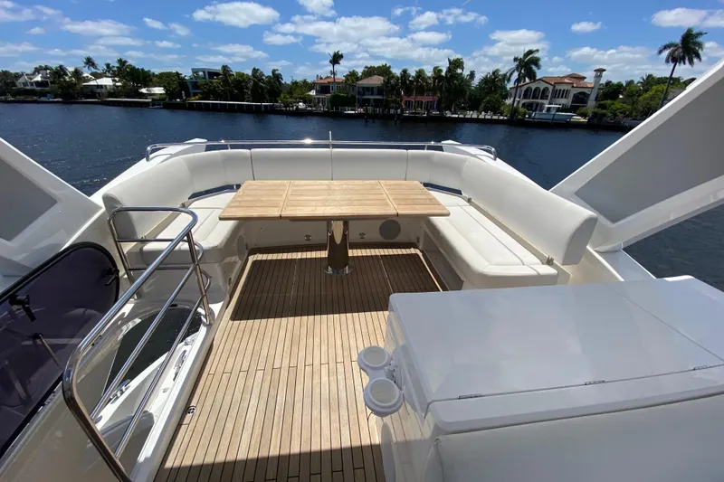 Slide: The Image of 2017 Sunseeker Manhattan 52 yacht deck with seating and table, overlooking water and palm trees. - 11