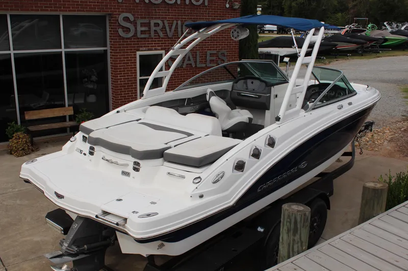 Slide: The Image of 2015 Chaparral 226 SSi boat with white and blue exterior, docked near a service building. - 4
