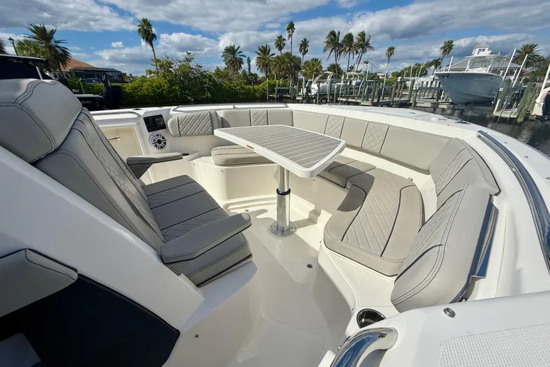 Slide: The Image of 2023 Pursuit S 358 Sport boat interior with luxurious seating and table, docked near palm trees. - 50