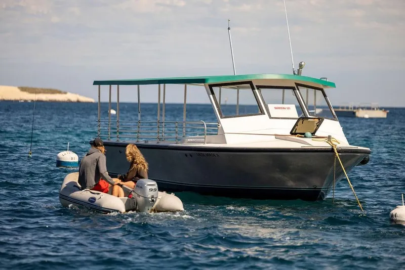 Slide: The Image of 2018 Seahawk Island Hopper boat anchored in blue ocean with two people approaching in a dinghy. - 2