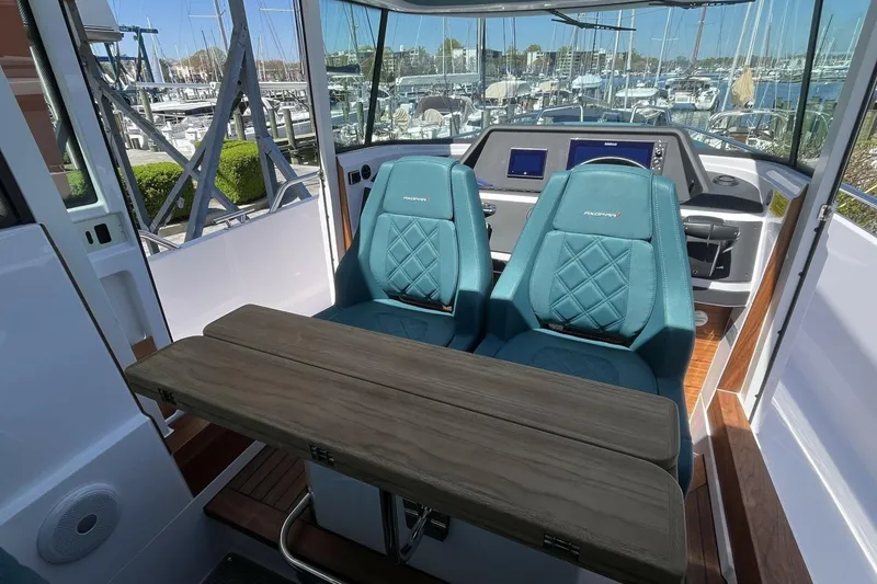 Slide: The Image of 2023 Axopar 28 Cabin interior with teal seats and wooden table, marina view. - 38