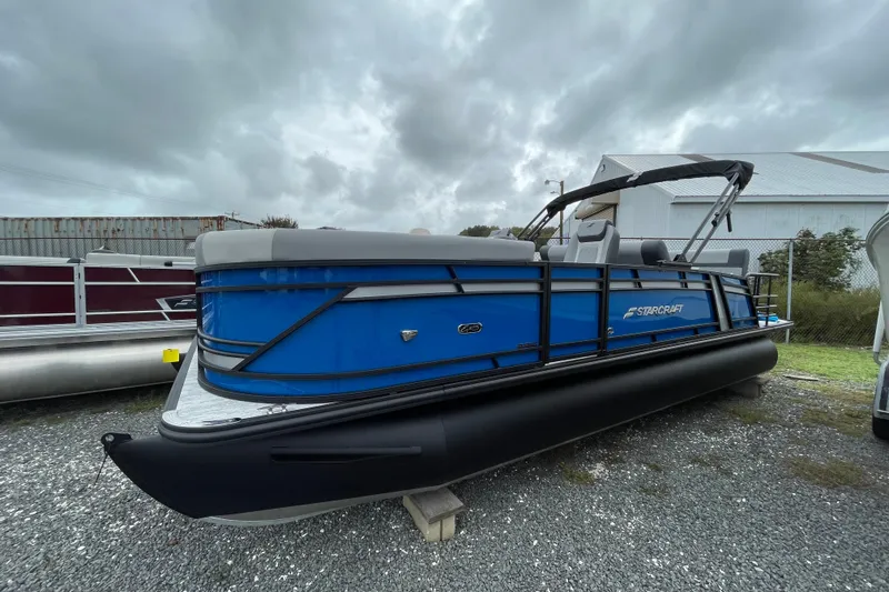 Slide: The Image of 2026 Starcraft EXS 3 DL pontoon boat, blue and black design, parked outdoors. - 0