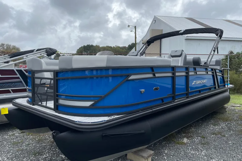 Slide: The Image of 2026 Starcraft EXS 3 DL pontoon boat with blue and black design, parked outdoors. - 1
