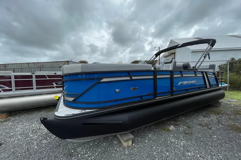 Slide: The Image of 2026 Starcraft EXS 3 DL pontoon boat with blue and black design, parked outdoors. - 11