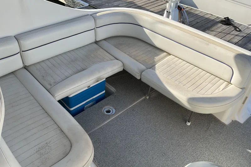 Slide: The Image of 2003 Bayliner 3055 Ciera boat seating area with white cushioned benches and a blue cooler. - 6