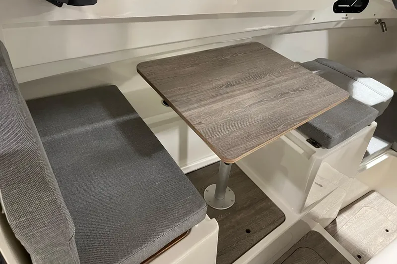 Slide: The Image of Interior seating area of 2026 Bayliner Trophy T23 Explorer with wooden table and gray cushions. - 9