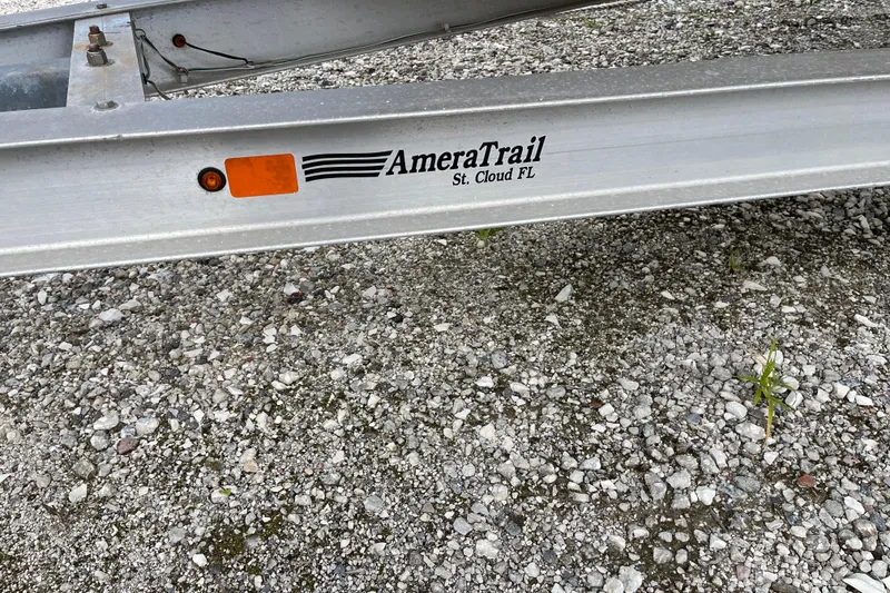 Slide: The Image of Trailer with AmeraTrail branding, supporting a 2014 ShearWater 23TE boat, on gravel surface. - 33