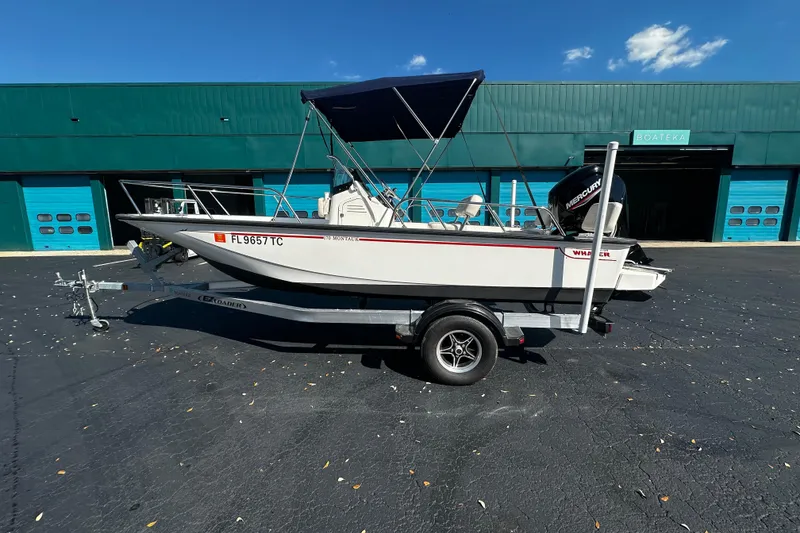 Slide: The Image of 2022 Boston Whaler 170 Montauk boat on trailer, parked outside a teal building. - 2