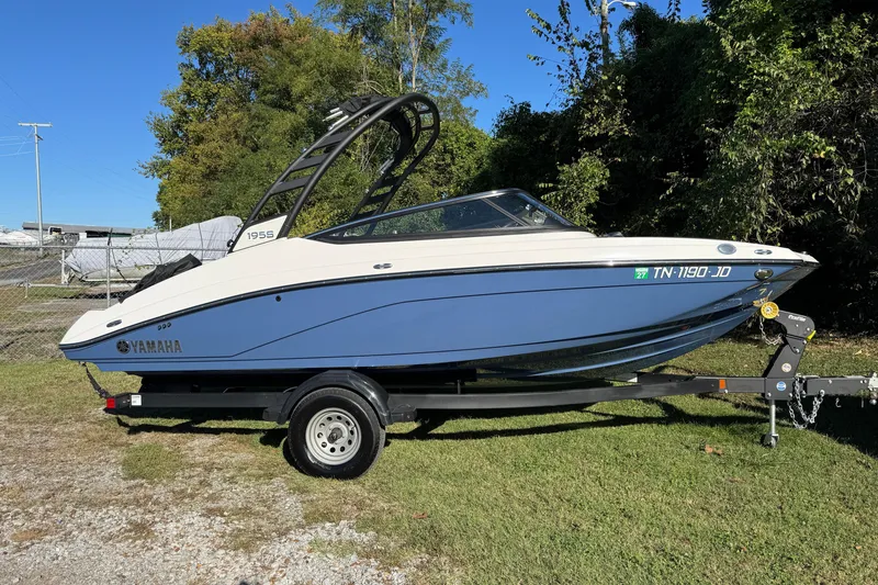 The Image of 2024 Yamaha Boats 195S on trailer, parked on grass, with trees in background. - 1