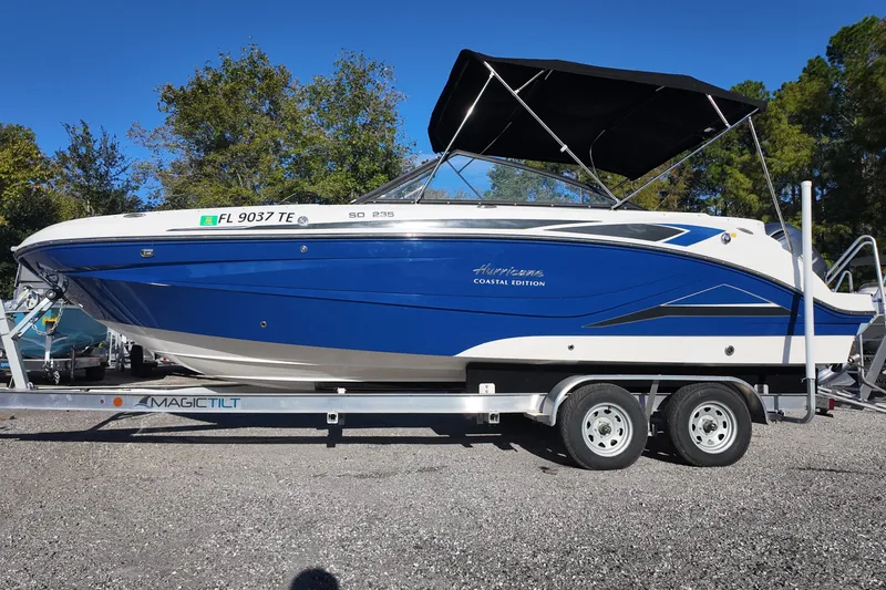 Slide: The Image of 2022 Hurricane SunDeck 235 OB boat on trailer, blue and white design, parked outdoors. - 2