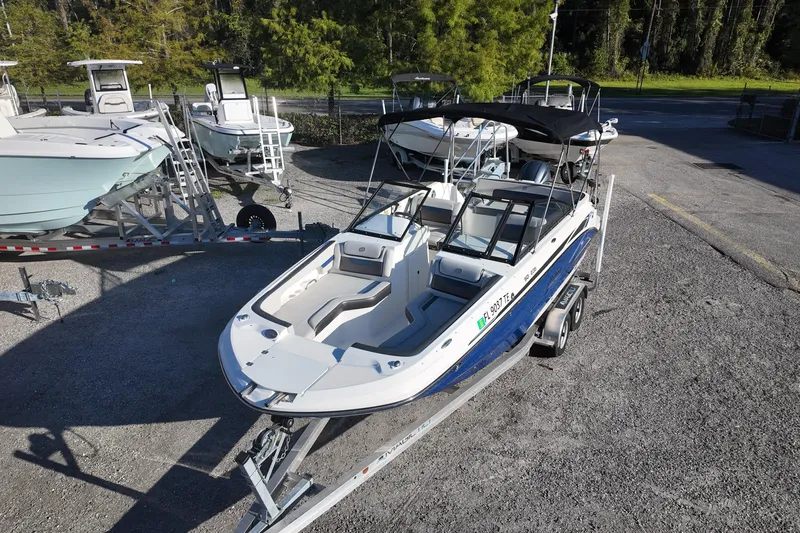 Slide: The Image of 2022 Hurricane SunDeck 235 OB boat on trailer, parked outdoors, surrounded by trees and other boats. - 6