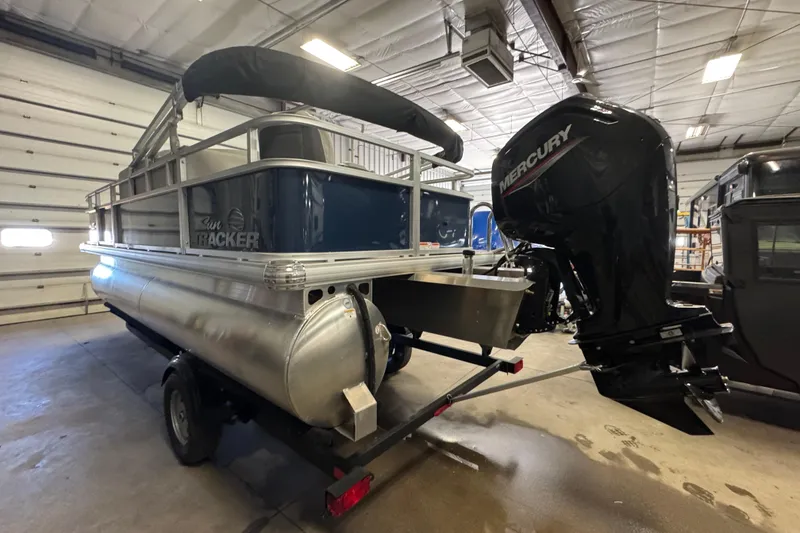 Slide: The Image of 2026 Sun Tracker Bass Buggy 18 DLX pontoon boat with Mercury outboard motor in a garage. - 5
