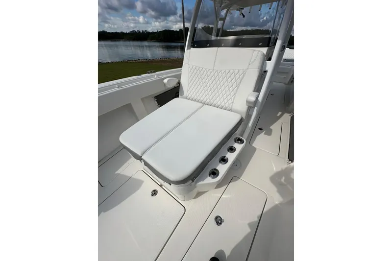 Slide: The Image of 2022 Fountain 38 CC LS boat with white cushioned seating and cup holders, docked by a lake. - 16